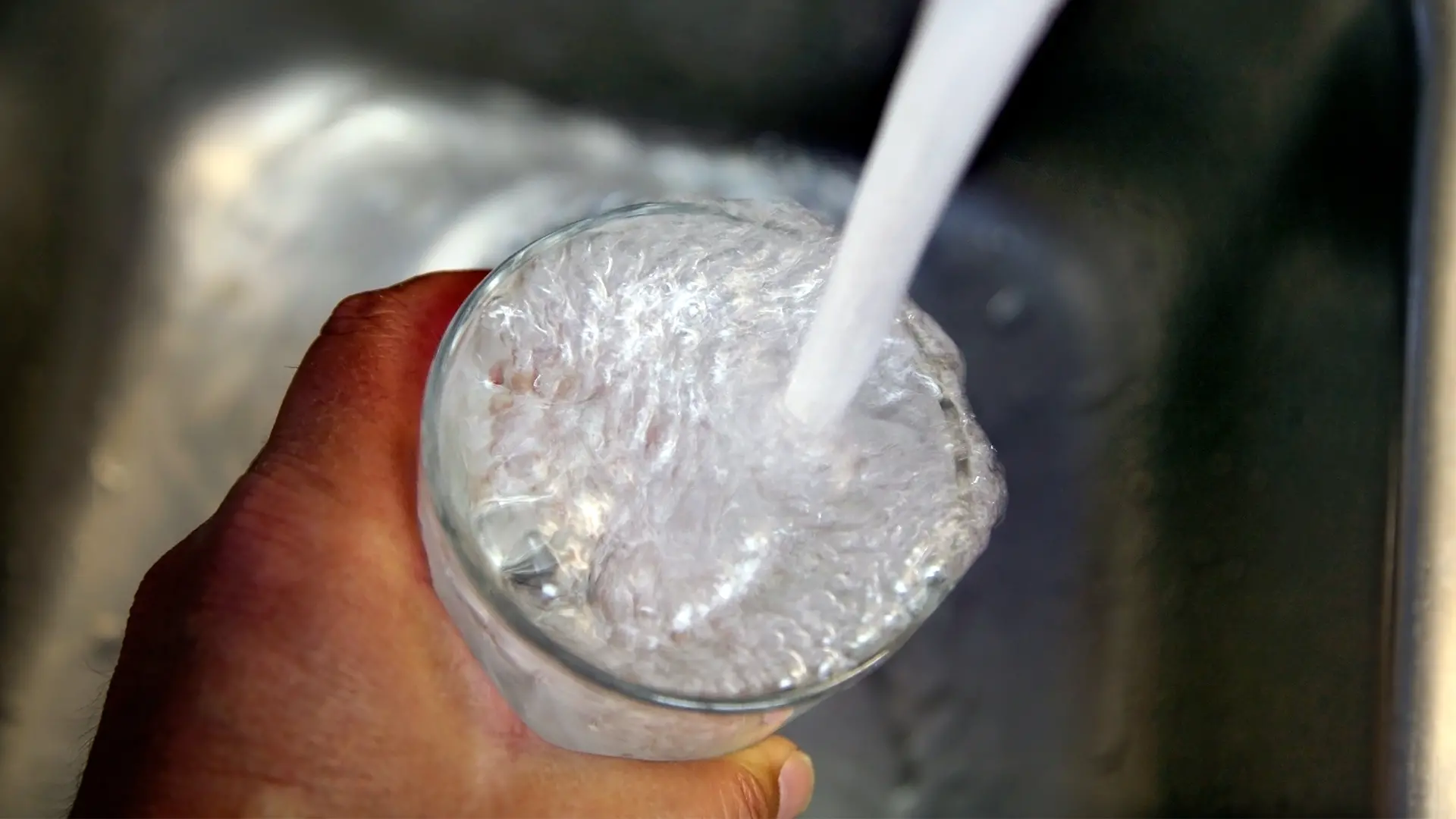 En hand håller i ett glas som fylls på med vatten från kranen.